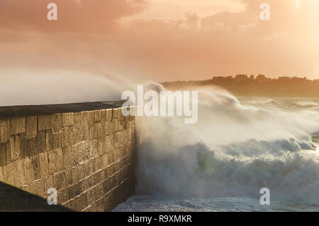 De grosses vagues sur la jetée de concassage de pierre courbe, sur un temps orageux avec des coucher de soleil, grande marée, Saint Malo, France. Banque D'Images