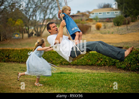 Jeune fille en poussant son père et sa petite sœur sur une balançoire en bois. Banque D'Images