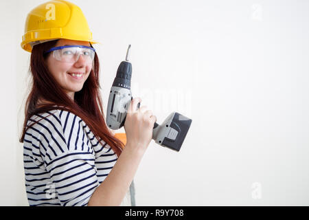 La photo d'une femme en casque jaune avec la perceuse à main dans l'appartement Banque D'Images