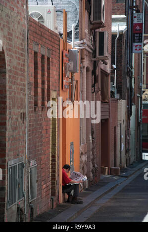Un homme est assis, lecture seule, dans une porte sur la Place, un Chinatown Waratah laneway entre Lonsdale et Little Bourke Streets, Melbourne Banque D'Images