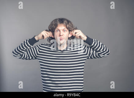 Man making silly monkey face isolé sur fond gris. Guy grimaces singe. Homme drôle maintenant ses oreilles et montre de la langue ressemble à monkey, prétendre Banque D'Images