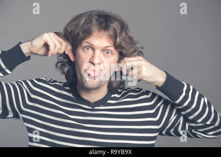 Close up of man making silly monkey face isolé sur fond gris. Guy grimaces singe. Homme drôle maintenant ses oreilles et montre de la langue ressemble à mon Banque D'Images