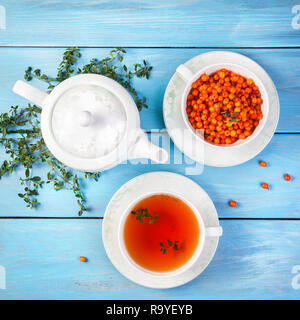 Thé de fines herbes et de baies dans la tasse près de la théière et les feuilles de thym on blue background Banque D'Images