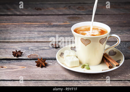 Indian Masala thé avec du lait, de la cannelle, badiane et cardamome épices en tasse avec des coeurs sur table en bois Banque D'Images