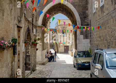 Drapeaux colorés accrocher au-dessus d'une rue de Casertavecchia, Italie. Un groupe de personnes parle ci-dessous de l'arcade le clocher de cette ville médiévale. Banque D'Images