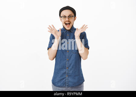 Portrait de l'homme Discours de perdre l'excitation et de sensations fortes secousses soulevées palms de surprise et de stupéfaction haletant avec bouche ouverte et yeux étonnés sur fond gris dans le quartier branché de black beanie Banque D'Images