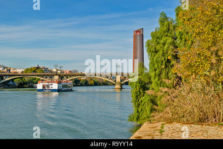 Espagne Séville Séville OU LA TOUR CAJASOL AVEC BATEAU DE TOURISME SUR LA RIVIÈRE GUADALQUIVIR, qui passe sous le pont en arc métallique de Triana Banque D'Images