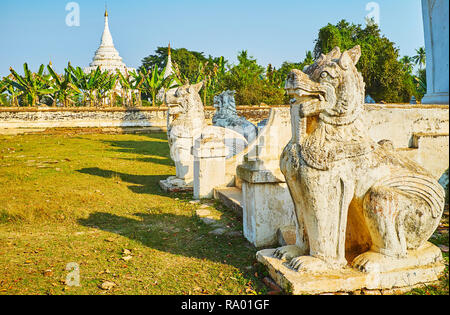 La vieille statues sculptées de chinthe - leoryphs Desada birman mythique garde Taya temple, la Pagode blanche de l'immeuble est visible derrière le jardin de banane o Banque D'Images