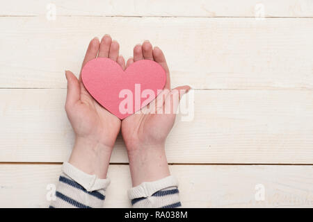 Les mains tenant papier rouge coeur. Womans palms avec symbole de l'amour sur vintage background with copy space. L'amour et la Saint-Valentin concept. Poignée d'amour, Close up. Banque D'Images
