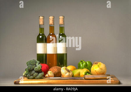 Assortiment de légumes sur une planche à découper, une rangée de 3 bouteilles d'huile de cuisson infusé. L'ail, le romarin, Banque D'Images