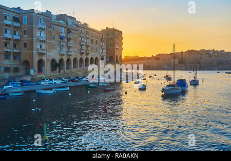 Le Fiery ciel au-dessus de la Valette Grand Port avec une vue sur les édifices médiévaux de Senglea, murs de La Valette et des bateaux de pêche de Vittoriosa marina, Malte. Banque D'Images