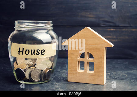 Un bocal de verre avec des pièces de monnaie et une maison en bois et l'inscription 'House'. L'accumulation de l'argent pour acheter une maison. Louer un appartement. Acheter une maison. Banque D'Images
