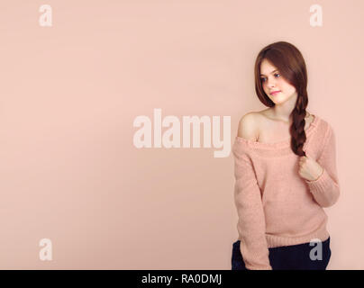 Brown-haired girl holding timide une tresse à la main sur un fond rose Banque D'Images