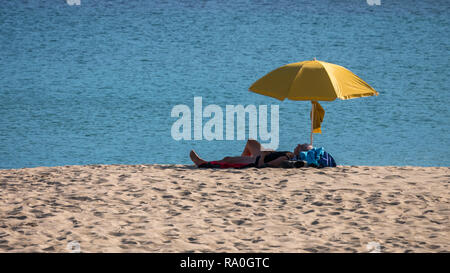 Une femme âgée lors de beau temps à la fin de l'été faire la sieste sous un parasol jaune sur une plage solitaire ; Sardineiro, Fisterra, Galice, Espagne Banque D'Images