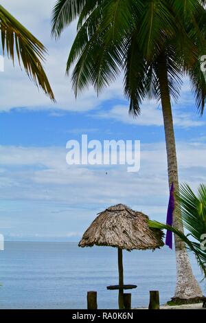 Le dirigeant d'une table et des chaises sous un palapa au toit de chaume et de palmiers en fin d'après-midi sur une plage des Caraïbes. Banque D'Images