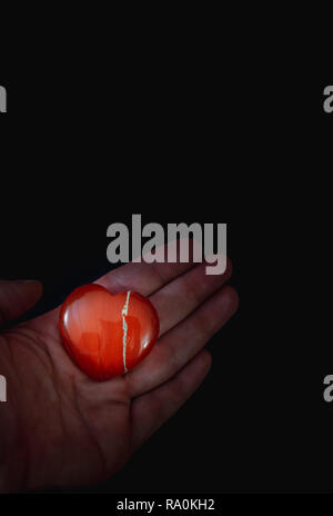 Un cœur rouge tenue en pierre dans une main sur fond noir - Love concept Banque D'Images