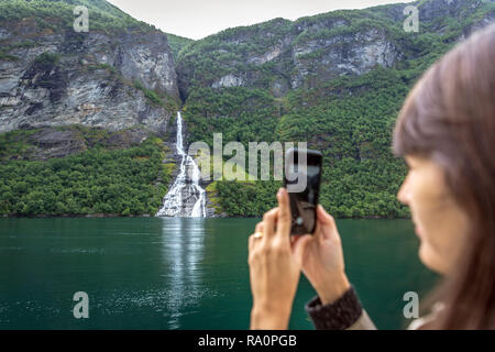 Les fjords, la Norvège - 5 juin 2018 - Jeune femme tenant un mobile photo d'une cascade dans les fjords de Norvège Banque D'Images