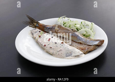 Close up partie de hareng mariné filets de poisson salé, avec des oignons et de la sauce sur plaque blanche sur le tableau noir, high angle view Banque D'Images