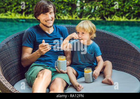 Père et fils manger le dessert avec chia seeds et de mangues à la piscine le matin. la saine alimentation, l'alimentation, les régimes végétariens et personnes concept Banque D'Images
