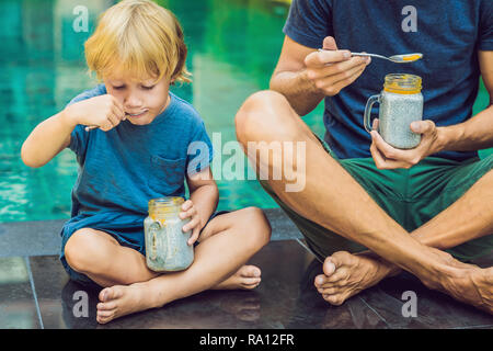 Père et fils manger le dessert avec chia seeds et de mangues à la piscine le matin. la saine alimentation, l'alimentation, les régimes végétariens et personnes concept Banque D'Images