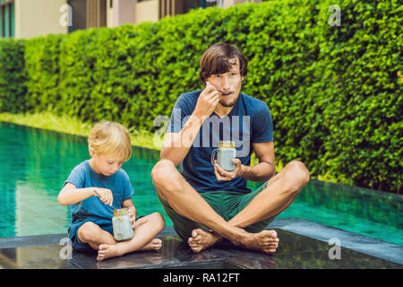 Père et fils manger le dessert avec chia seeds et de mangues à la piscine le matin. la saine alimentation, l'alimentation, les régimes végétariens et personnes concept Banque D'Images