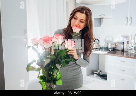 Des roses rose femme met dans un vase de fleurs odorantes. Jeune femme au foyer en prenant soin de confort dans la cuisine. Conception de la cuisine moderne. Cuisine blanc et argent Banque D'Images