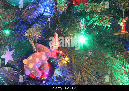 Une vue étroite d'un vert feuilles arbre de Noël avec des lumières électriques, décorations ornements suspendus et le Père Noël dans une ambiance aux couleurs lumineuses Banque D'Images