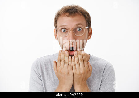 Close-up shot of impressionné choqué et fasciné charmant homme de race blanche avec barbe en disant lunettes pliantes wow bouche ouverte et holding palms au-dessus de la lèvre d'être préoccupé et stupéfait Banque D'Images