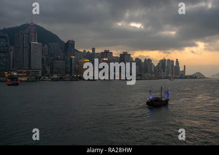 Les jonques touristiques bien éclairé dans le port de Victoria sous la toile de gratte-ciel scintillants, alors que le soleil se couche sur Kennedy Town, Hong Kong Banque D'Images