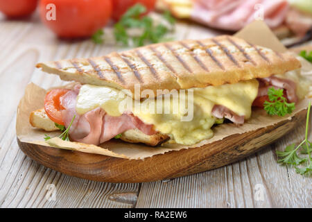 Toast grillé et enfoncé avec jambon fumé, fromage, tomate et laitue sandwich servi sur une table de bois sur papier Banque D'Images