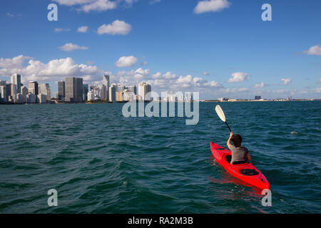 Fille d'aventure Kayak en face d'un paysage urbain du centre-ville moderne au cours d'une soirée ensoleillée. Prises à Miami, Floride, États-Unis d'Amérique. Banque D'Images