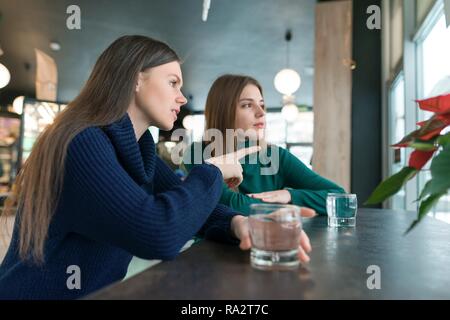 Parler de jeunes femmes, filles assis dans cafe sourire et parler, de boire de l'eau dans le verre, en regardant par la fenêtre. Banque D'Images