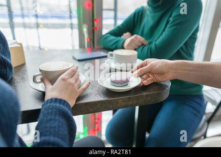 Close-up de deux femmes mains avec tasses de café et macarons sur la plaque dans la main de l'homme sur la table de pierre grise, café, arrière-plan. Banque D'Images