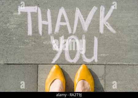 Pieds femelles avec texte merci écrit sur le trottoir gris. Banque D'Images