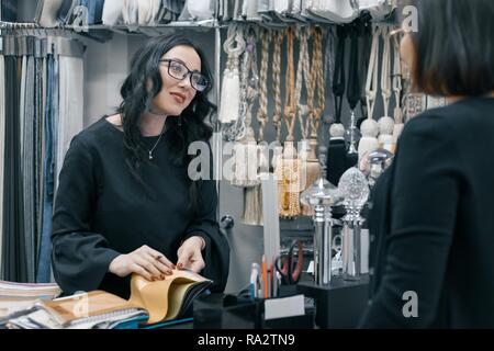 Les femmes en milieu de travail designer, business woman in lunettes avec stylo et bloc-notes échantillon du tissu travaillant dans le bureau. Concepteur de femmes à la recherche et de parler Banque D'Images