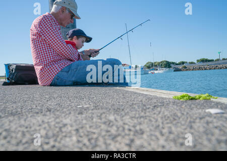 Grand-père et petit-fils assis ensemble à la pêche sur la jetée de calme matinée ensoleillée. Banque D'Images