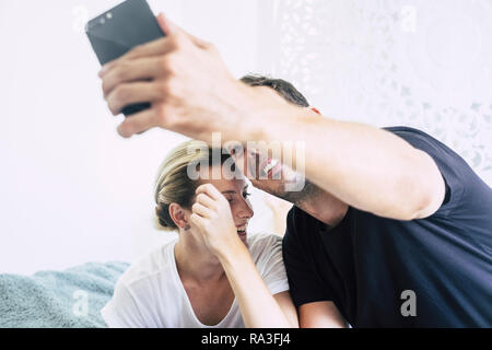 Beau jeune couple millénaire caucasian blonde et les cheveux noirs s'amuser et rire en tenant une conversation vidéo ou selfies avec téléphone mobile - et de la technologie Banque D'Images