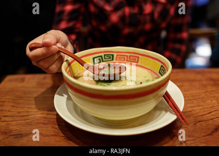 Femme est titulaire d'une cuillère tout en mangeant un bol de ramen, Tokyo, Japon Banque D'Images