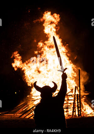 Une personne en costume Viking en face d'un bateau viking brûlant pendant la fête du Feu, Flamborough Viking un défilé à thème, le Nouvel An, à Flamborough près de Bridlington, Yorkshire, au profit d'organismes de bienfaisance et des groupes communautaires locaux. Banque D'Images