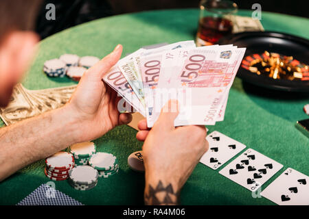 Image recadrée de tattooed man holding euro banknotes at poker table in casino Banque D'Images