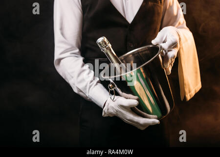 Portrait of waiter holding bouteille d'alcool dans le seau à champagne sur noir Banque D'Images