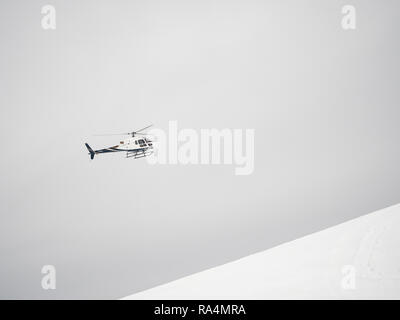 Hélicoptère Blanc survole les montagnes enneigées sur un jour nuageux Banque D'Images