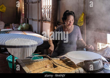 Vietnamienne à l'aide de grains de riz pour faire le papier de riz s'enroule dans un atelier de démonstration. Tiền Giang à Cai Be, Province, Delta du Mékong, Vietnam, Asie Banque D'Images