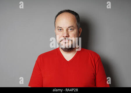 Homme d'âge moyen dans son 40s portant des t-shirt avec des cheveux noirs courts et barbe grisonnante souriant - gray wall background with copy space Banque D'Images