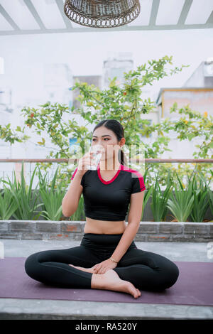 Young Asian woman à partir du verre de l'eau potable après l'exercice, le yoga et la méditation Banque D'Images