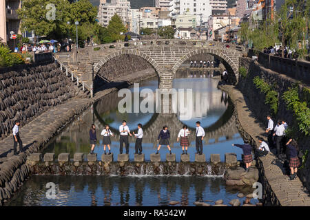 Nagasaki, Japon - 25 octobre 2018 : Les élèves de marcher sur des pierres dans les Nakashima rivière devant l'Meganebashi Banque D'Images