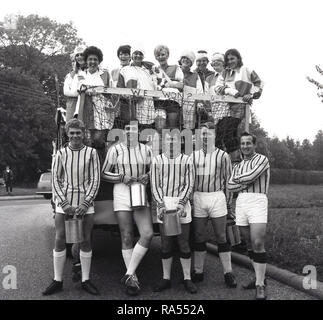 1965, historique, joueurs masculins d'une équipe de football dans leur kit, avec les femmes de partisans sur un flotteur debout au-dessus d'eux, tous les participants à un carnaval, England, UK, Banque D'Images