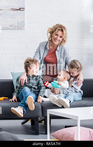 Happy mother smiling at camera tout en passant du temps avec trois adorables enfants à la maison Banque D'Images