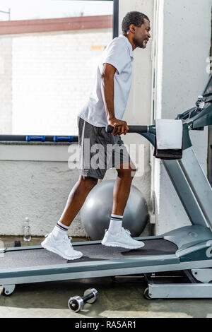 Vue latérale d'african american man running sur tapis roulant à la salle de sport Banque D'Images