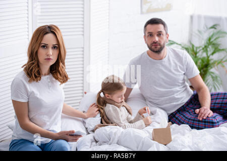 Les parents inquiets assis près de fille malade dans la chambre et looking at camera Banque D'Images